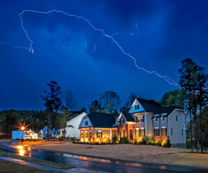 A bolt of lightning illuminates the night sky over a residential neighborhood.